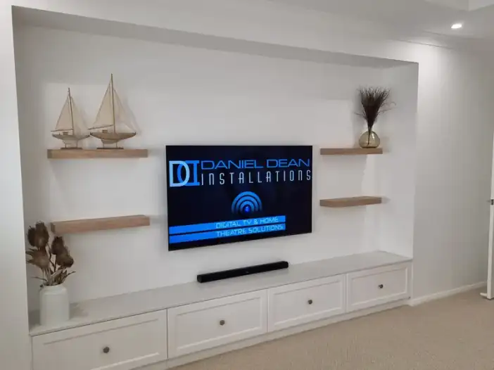 A wall-mounted television between floating shelves above a white cabinet