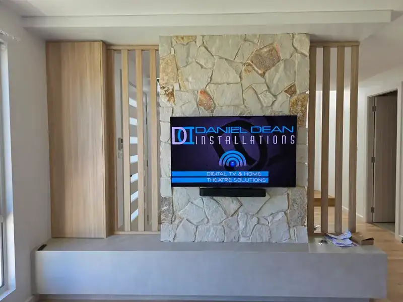A television wall-mounted on a stone feature wall with a soundbar below and no visible cables